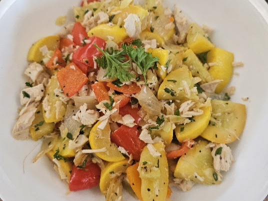 A colorful chicken and summer squash skillet with peppers and fresh herbs served in a white bowl.